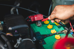 Eine Hand prüft die Spannung einer Autobatterie mit einem Multimeter im Motorraum. Ein wichtiger Tipp aus dem Auto Batterie leer Ratgeber, um die Ursache einer leeren Batterie zu finden.
