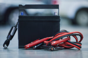 Eine Autobatterie steht neben Starthilfekabeln und einem Werkzeug, bereit für eine Starthilfe. Dieser Tipp aus dem Auto Batterie leer Ratgeber zeigt die Vorbereitung für den Fall einer leeren Batterie.