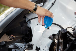 Eine Person füllt Scheibenwaschflüssigkeit mit einem Trichter in den Vorratsbehälter eines Autos. Der Auto Flüssigkeiten prüfen Ratgeber empfiehlt, den Füllstand der Waschflüssigkeit zu überprüfen.
