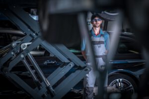 Ein Mechaniker steht in einer Werkstatt vor einem Auto auf der Hebebühne, bereit für den Bremsflüssigkeitswechsel. Der Bremsflüssigkeit wechseln Tipps Ratgeber empfiehlt professionelle Unterstützung.
