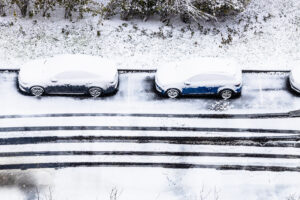 Mehrere Autos stehen verschneit auf einem Parkplatz, umgeben von Schnee und Eis. Die Szene zeigt die Bedeutung der Vorbereitung für Fahrsicherheit bei Regen und Schnee.