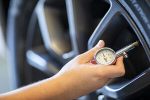 Eine Hand überprüft den Reifendruck an einem Autoreifen mit einem Manometer. Ein wichtiger Tipp aus dem Reifen Lebensdauer verlängern Ratgeber, um den Verschleiß zu minimieren.
