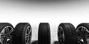Mehrere Autoreifen mit unterschiedlichen Profilen stehen auf trockenem, rissigem Boden. Der Sommer- und Winterreifen Unterschiede Ratgeber erklärt die verschiedenen Reifenarten.
